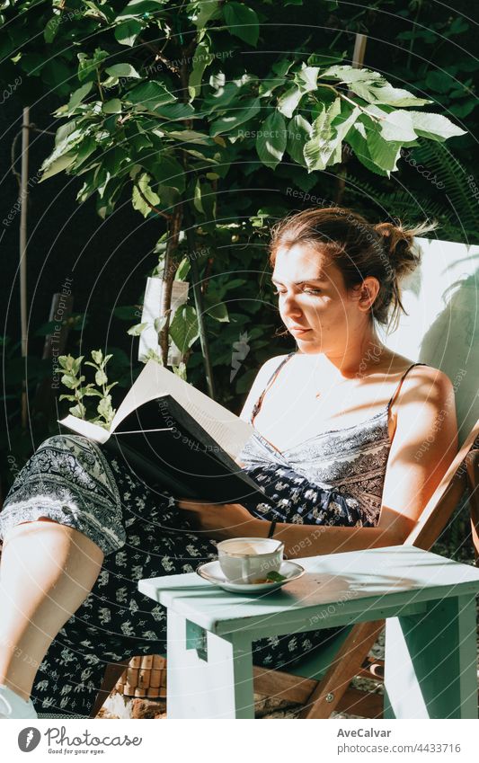 Frau liest ein Buch, während sie sich an einem sonnigen Tag auf einem Stuhl zurücklehnt, Kopierraum, Entspannungs- und Hobbykonzepte, soziales Netzwerk lesen