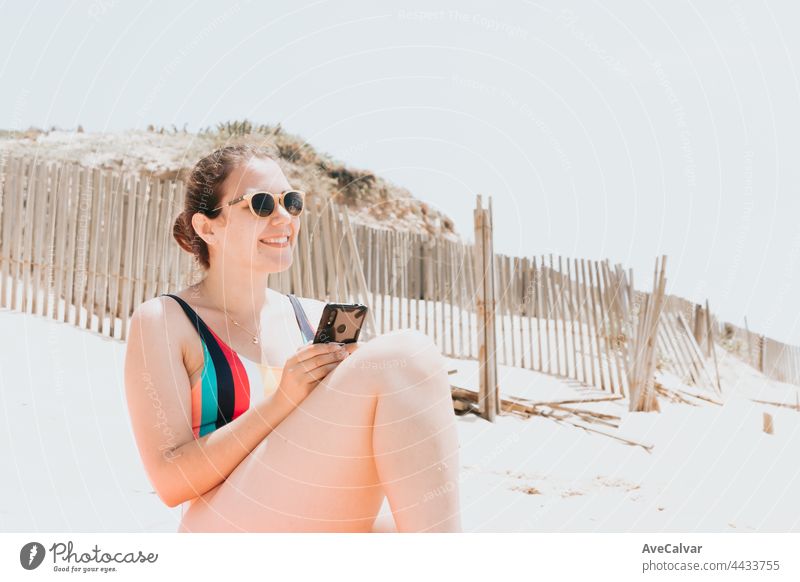 Junge Frau lächelt beim Chatten am Telefon trägt einen bunten Badeanzug am Strand ein Sonnenbad nehmen, Reisen jungen Urlaub Konzept, Kopie Raum, soziales Netzwerk, Sonnenbrille Benutzer Konzept