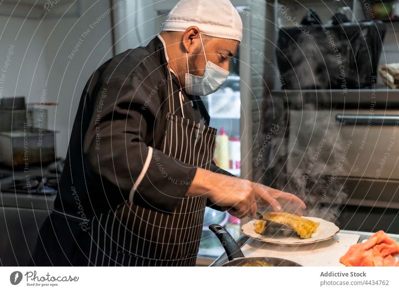 Ethnischer Koch, der in der Küche leckere Cannelloni auf den Teller bringt Küchenchef Spätzle heiß Speise Lebensmittel Verdunstung vorbereiten Mann diffus