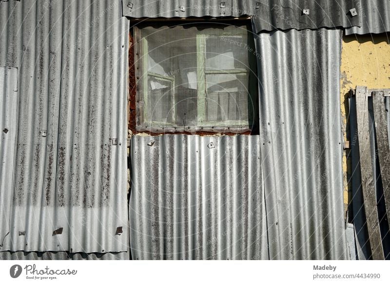 Altes Holzfenster mit Insektengitter in alter silbergrauer Wellblechfassade eines Wohnhaus im Sommer bei Sonnenschein im Dorf Maksudiye bei Adapazari in der Provinz Sakarya in der Türkei