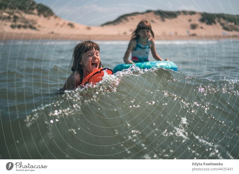 Zwei kleine Mädchen schwimmen im Meer Schwimmsport Wellen MEER Strand Sand Himmel Wasser aufblasbares Spielzeug aufblasbarer Ring Urlaub reisen aktiv Abenteuer