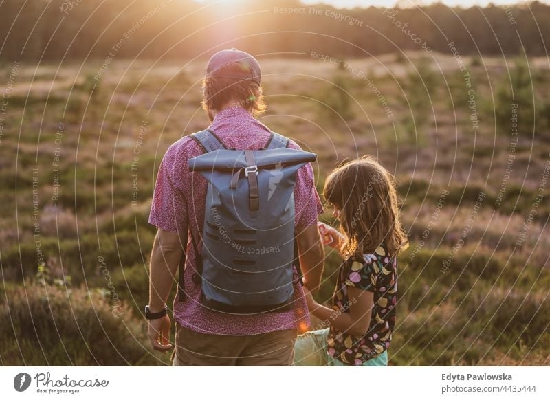 Vater und Tochter bei einer Wanderung im Wald bei Sonnenuntergang Zusammensein Eltern Liebe Rücken Rucksack Spaziergang Wiese Gras Feld ländlich Landschaft
