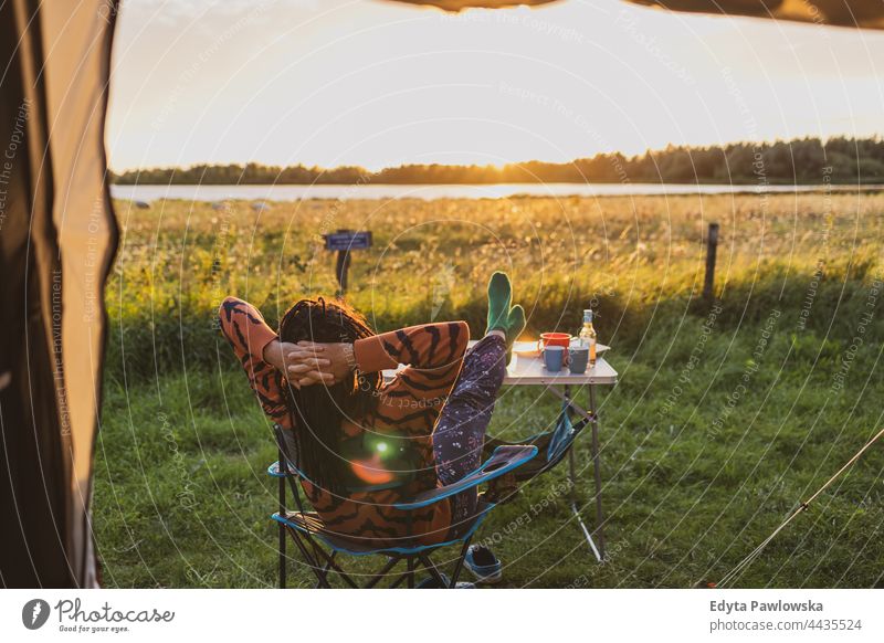 Frau entspannt sich bei Sonnenuntergang vor dem Zelt Campingplatz Wiese Gras Feld ländlich grün Landschaft Abenteuer wandern Wildnis wilder Urlaub reisen aktiv