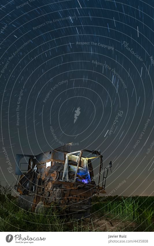 verschrotteter und verlassener Mähdrescher inmitten eines Maisfeldes, unter einem Sternenhimmel in einer klaren Nacht, Langzeitbelichtung Nachtfotografie