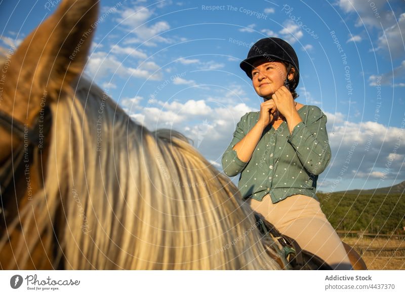 Nachdenkliche Frau auf einem Pferd unter bewölktem Himmel auf dem Lande Pferderücken Stute verträumt Schutzhelm behüten pferdeähnlich Tier wolkig Landschaft
