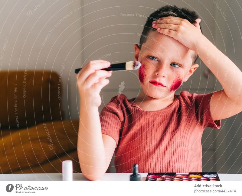Junge trägt im Haus Make-up auf das Gesicht auf Applikator Schönheit Kosmetik Tastkopf dekorativ unordentlich Spaß haben Porträt Kindheit Palette Produkt