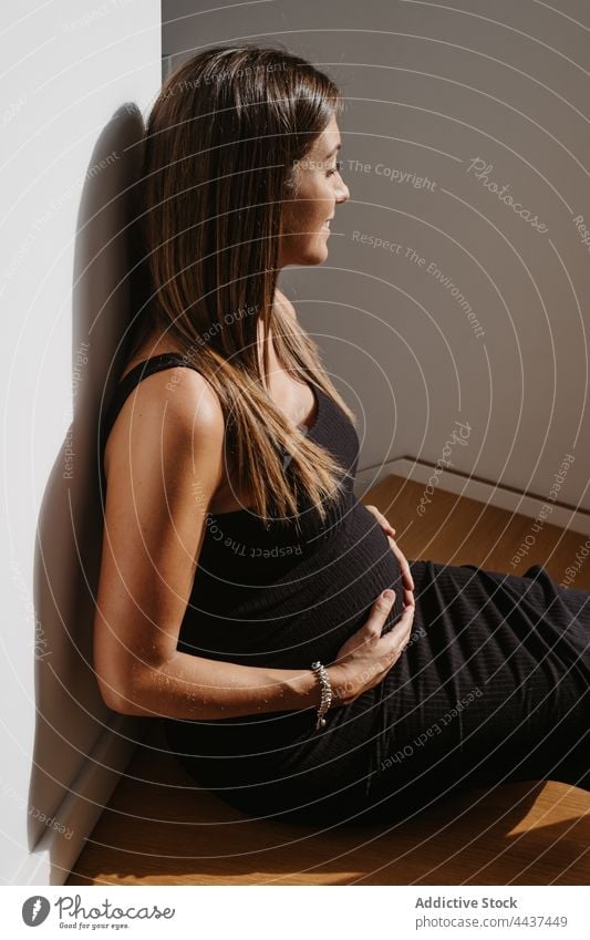 Lächelnde schwangere Frau berührt Bauch auf dem Boden zu Hause Bauch anfassen Schwangerschaft verträumt Augen geschlossen mütterlich warten vorwegnehmen