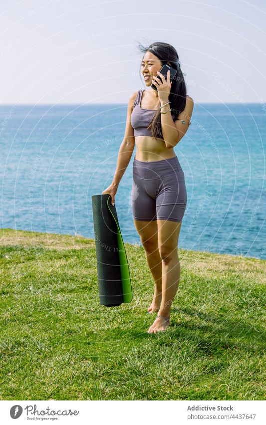 Lächelnde asiatische Frau, die am Meeresufer mit ihrem Smartphone spricht reden Yoga Wellness Gesunder Lebensstil Körper benutzend Apparatur Gerät Funktelefon