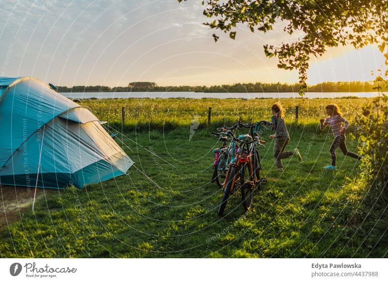 Spielende Kinder auf dem Campingplatz rennen spielerisch Spaß Freude Familie Zelt Fahrrad Fahrradfahren Wiese Gras Feld ländlich grün Landschaft Abenteuer