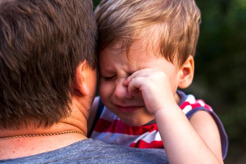 Ein kleiner Junge weint in den Armen seines Vaters und kuschelt sich an ihn, um sich beschützt zu fühlen. Ausdruck fürsorglich Weinen Partnerschaft Kind Sohn