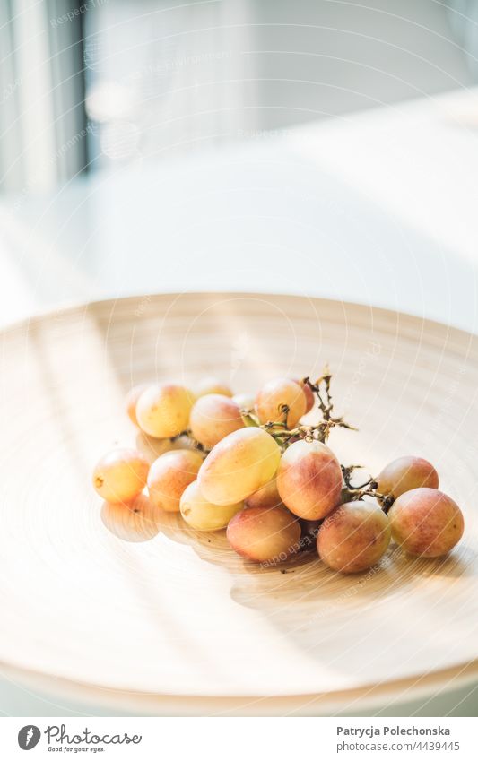 Süße Baumwolltrauben auf einem Holzteller auf einem weißen Tisch in einem Innenraum Trauben Zuckerwatte Stillleben Lebensmittel Frucht hölzern Teller