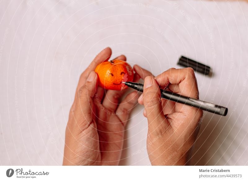 Draufsicht auf eine Frau, die mit den Händen ein Smiley-Gesicht auf eine Clementine zeichnet Clementinen-Orangen Smiley-Zeichnung Ansicht von oben Frauenhände