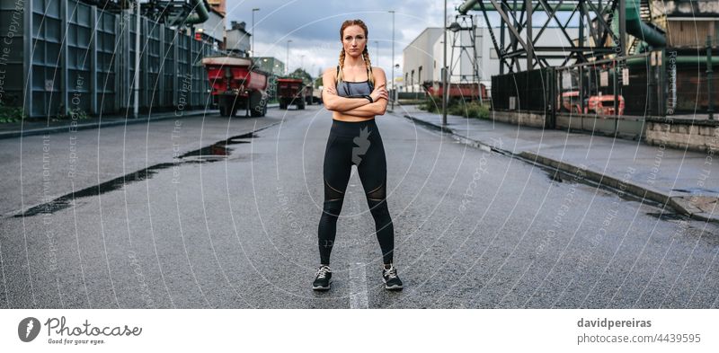 Sportlerin mit Blick auf die Kamera posiert vor einer Fabrik Frau Läufer schauende Kamera Mitte Straße Asphalt selbstbewußt verschränkte Arme Transparente Netz