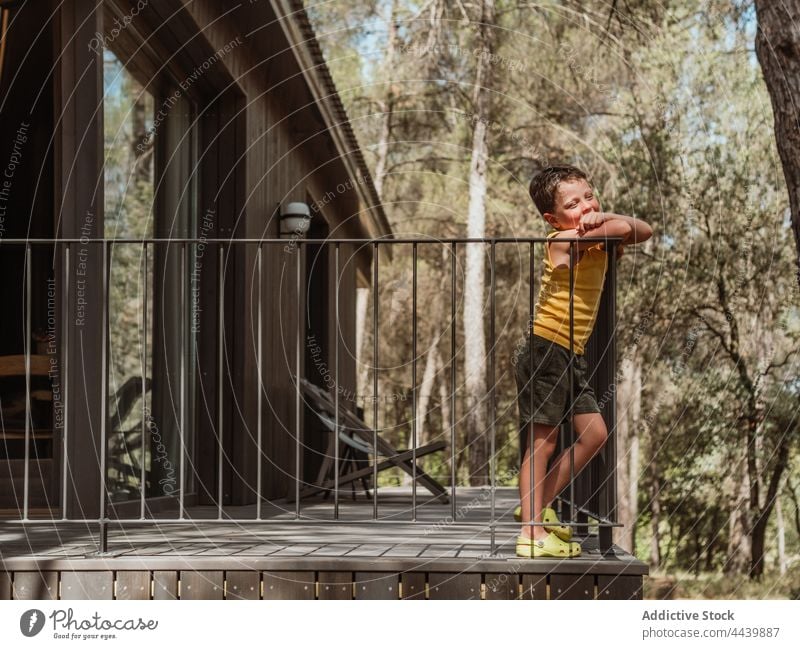 Kind steht auf der Terrasse eines Hauses im Wald Junge Veranda Erholung Sommer friedlich ruhig Natur hölzern Wälder Waldgebiet Sommerzeit sonnig Sonnenlicht
