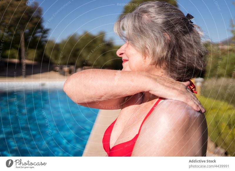 Lächelnde alte Frau, die sich beim Entspannen am Pool mit Lotion einschmiert Senior Sonnenbad Sonnencreme Sahne bewerben positiv Hydrat Kälte Beckenrand