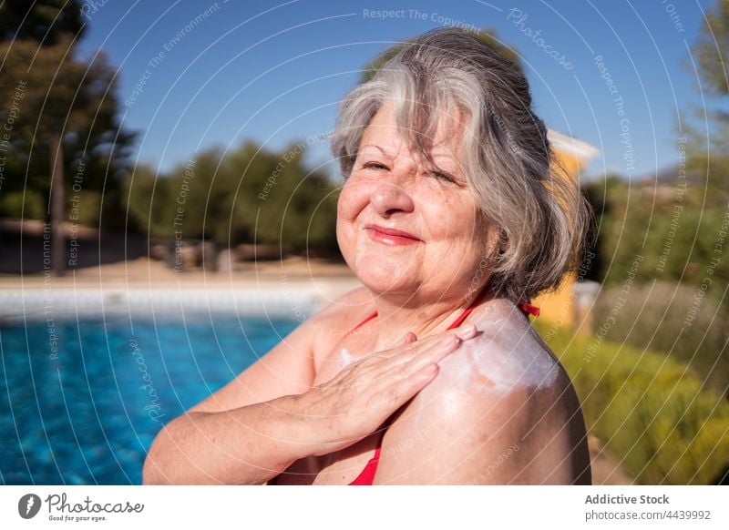 Lächelnde alte Frau, die sich beim Entspannen am Pool mit Lotion einschmiert Senior Sonnenbad Sonnencreme Sahne bewerben positiv Hydrat Kälte Beckenrand
