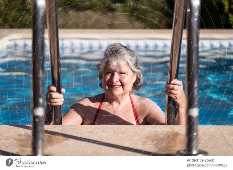 Lächelnde alte Frau, die sich an den Handläufen des Pools festhält, während sie sich im Wasser entspannt positiv Senior genießen Geländer Kälte