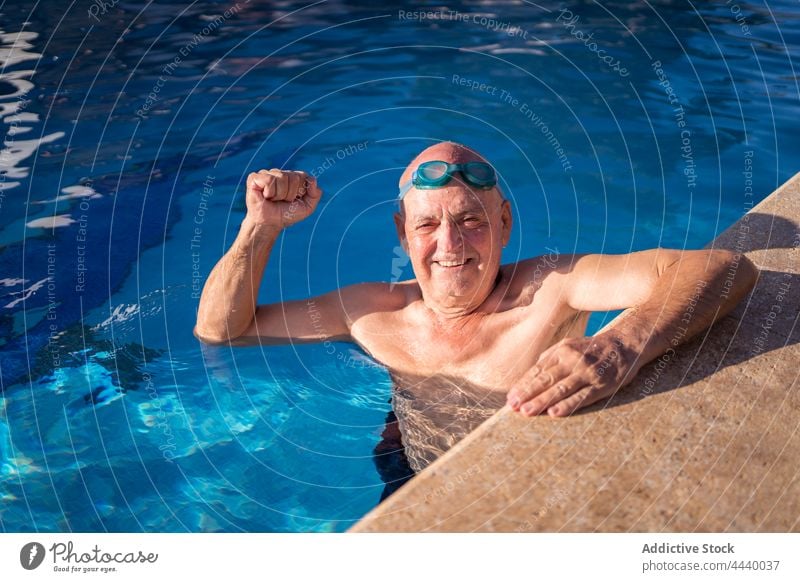 Alter Mann hebt die Faust beim Schwimmen im Pool Senior mit der Faust nach oben Kraft gestikulieren blau Wasser Zusammensein zeigen Arme hochgezogen