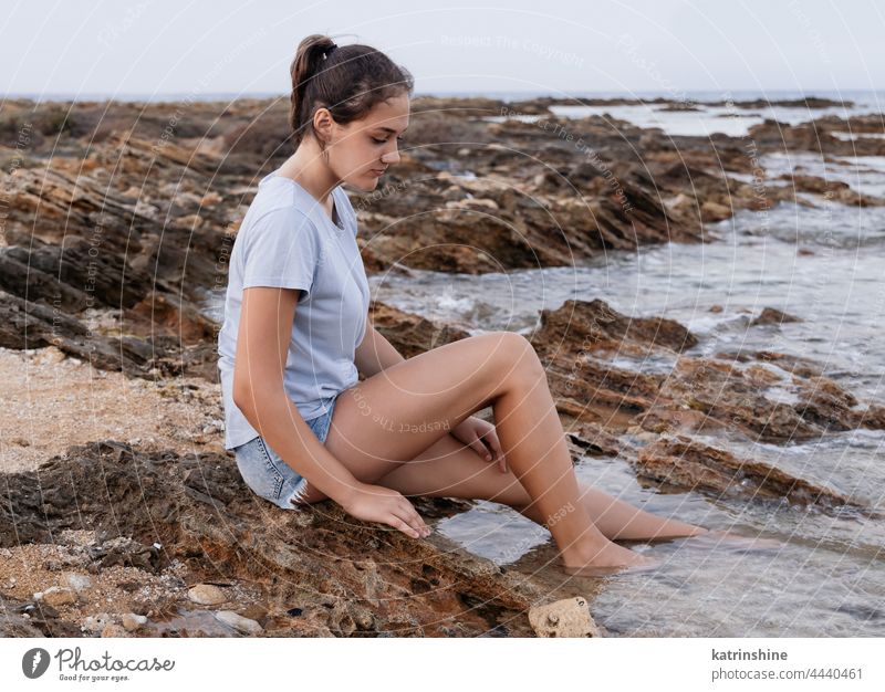 Teenager-Mädchen sitzt auf einer Klippe am Meer blau Kaukasier MEER sitzen Felsen Sonnenuntergang Jugendlicher Stein tragend Kindheit Frau Textfreiraum