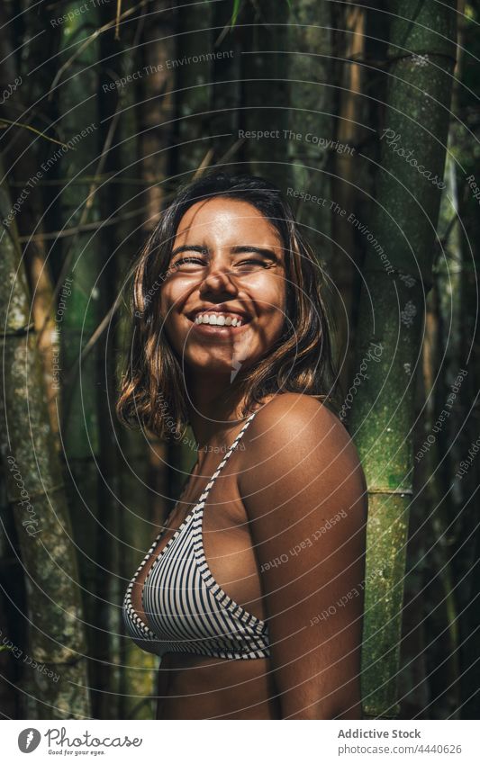 Lächelnder Tourist im Badeanzug vor Bambuspflanzen Reisender Badebekleidung Urlaub Ausflug herzlich natürlich Schatten Frau heiter Zweig Tourismus offen
