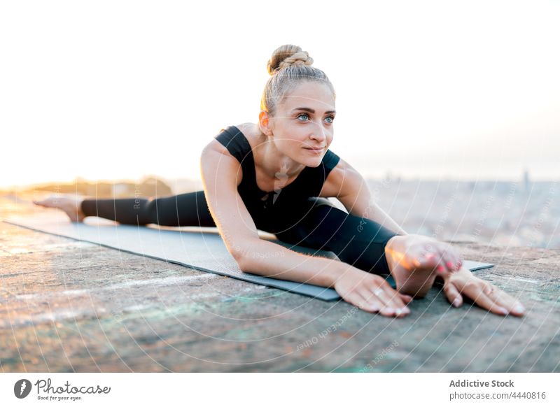 Flexible Frau in breiter Spagat-Pose auf Sportmatte weite Spaltungen Sprit Yoga Sonnenuntergang Körperhaltung Dachterrasse Dehnung Körperpflege beweglich Asana