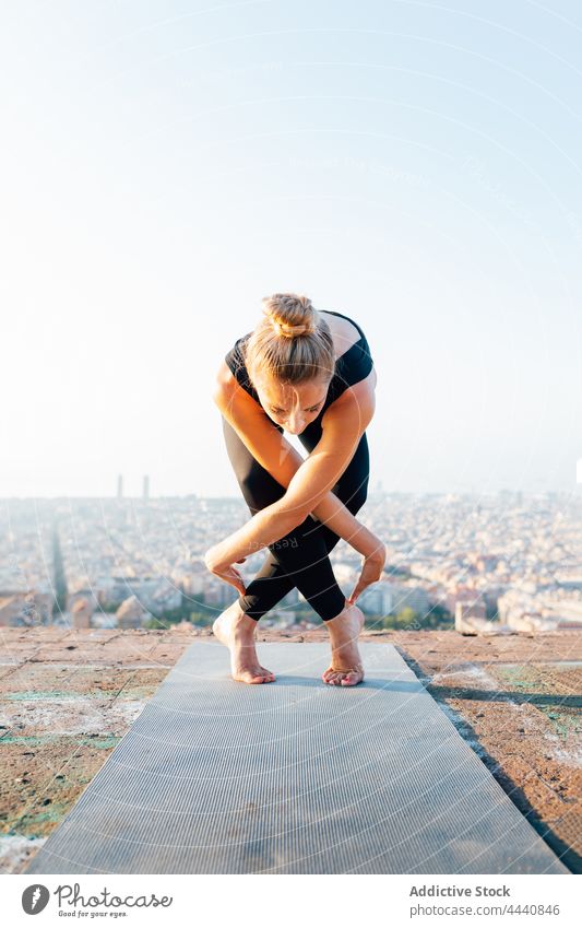 Frau übt Yoga auf Matte in der Stadt Vorwärtsbeuge Beine gekreuzt Wellness Gesunder Lebensstil Vitalität Energie üben Dachterrasse Großstadt vorbereiten Pose
