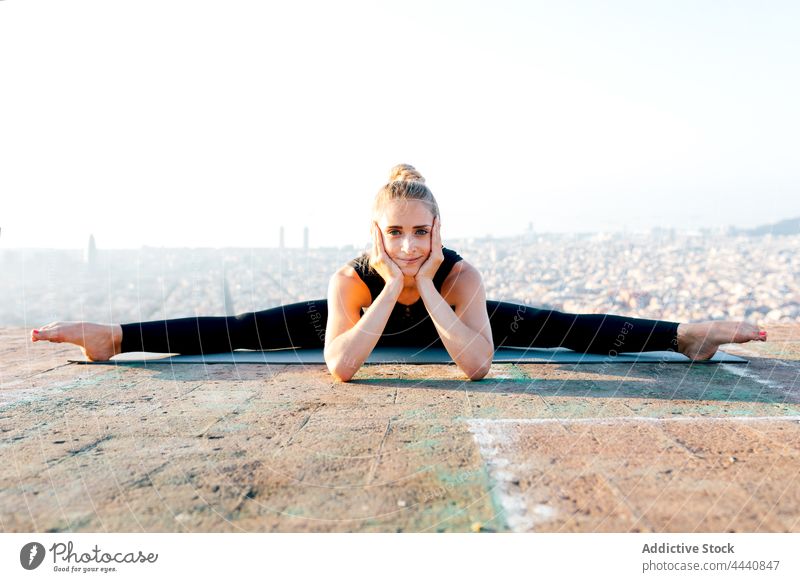 Flexible Frau in breiter Spagat-Pose auf Sportmatte weite Spaltungen Sprit Yoga Sonnenuntergang Körperhaltung Dachterrasse Dehnung Körperpflege beweglich Asana