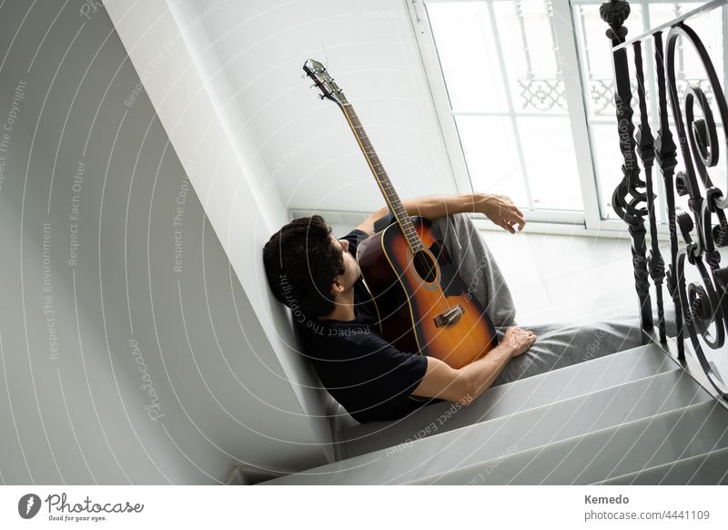 Ein nachdenklicher junger Mann auf einer Treppe macht eine Pause vom Gitarrenspiel. Musik Musiker Gitarrenspieler Person Inspiration Idee unbeseelt unmotiviert