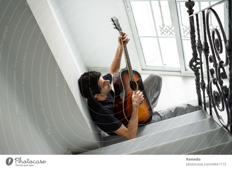 Entspannter junger Mann spielt Gitarre auf einer Treppe in der Nähe des Fensters. spielen Musik Treppenhaus Instrument akustisch Gitarrenspieler Hobby männlich