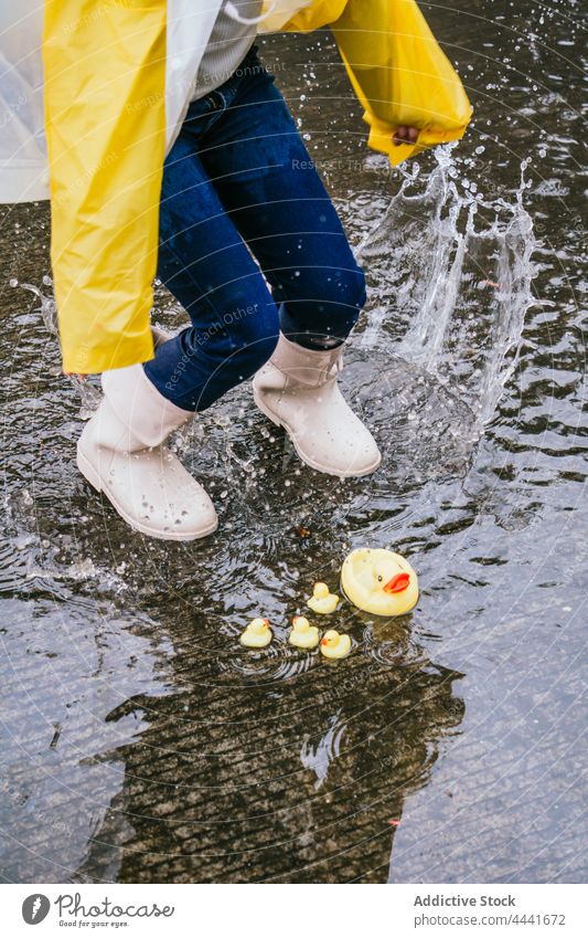 Crop-Mädchen in Gummistiefeln springt auf Pfütze mit spritzendem Wasser springen laufen Spaß haben spielerisch Ente platschen aktiv Energie