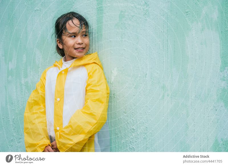 Lächelnde asiatische Mädchen stehen gegen raue Wand Regen heiter Kindheit genießen Regenmantel herzlich charmant ethnisch Inhalt nachdenken offen charismatisch