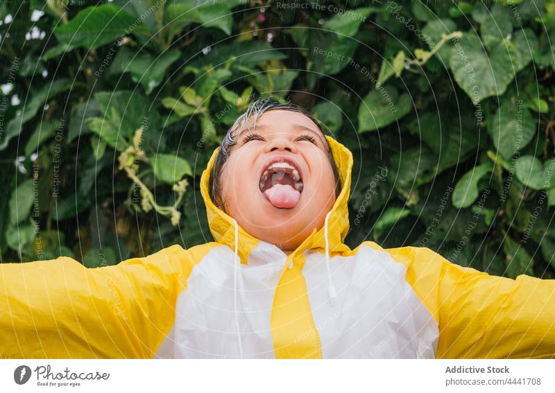 Glückliches asiatisches Mädchen trinkt Regen gegen Busch im Park trinken ausspannen Mund geöffnet Spaß haben Kindheit heiter sorgenfrei genießen Strauch