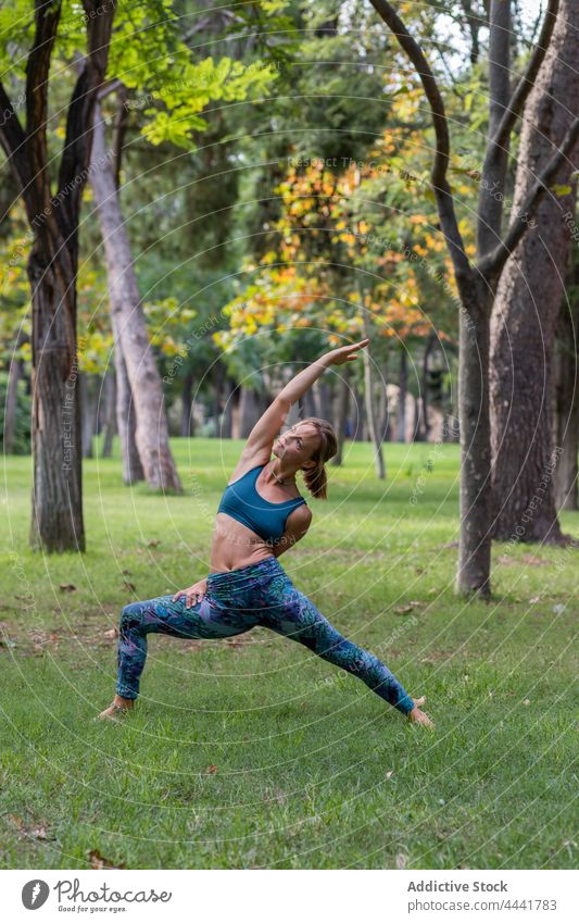Junge Frau bei der Durchführung von Exalted Crescent Lunge während der Yoga-Praxis im grünen Park Gras Dehnung Sportbekleidung beweglich Natur