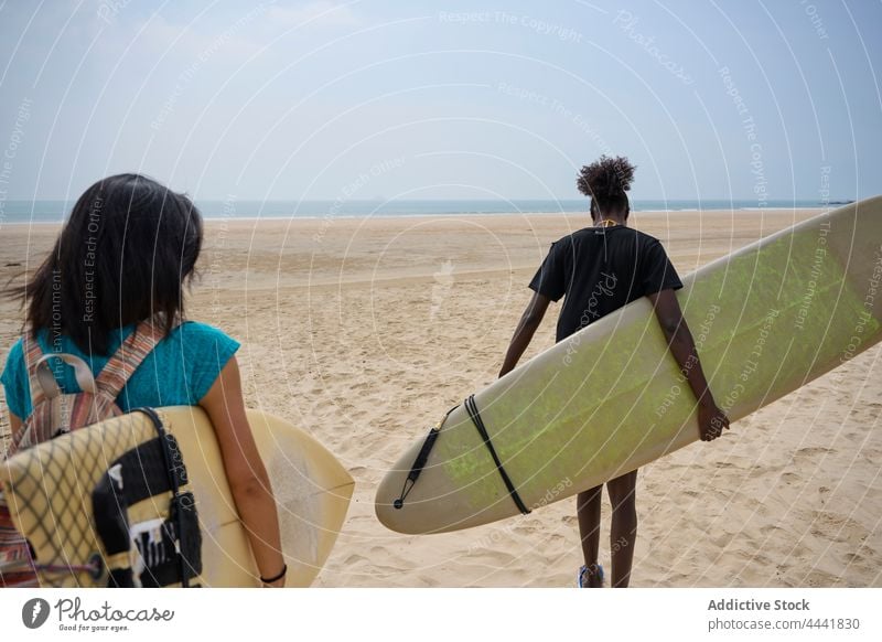 Verschiedene Sportlerinnen mit Surfbrettern unterhalten sich bei einem Spaziergang am Meer reden Freundschaft Surfen Zeit verbringen Ufer Blauer Himmel Frauen