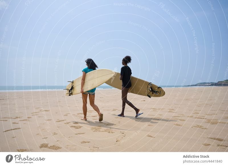 Verschiedene Sportlerinnen mit Surfbrettern unterhalten sich bei einem Spaziergang am Meer reden Freundschaft Surfen Zeit verbringen Ufer Blauer Himmel Frauen
