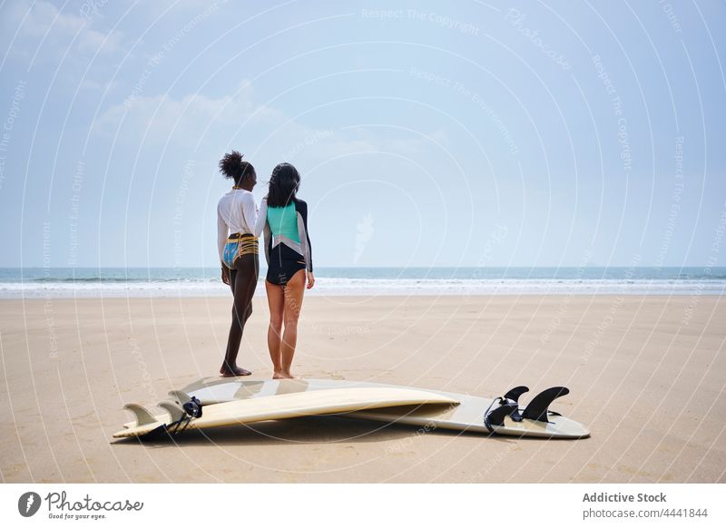 Lächelnde multirassische Freundinnen mit Surfbrettern am Meeresufer interagieren Longboard Sport Küste heiter Blauer Himmel Frauen Sportlerinnen reden