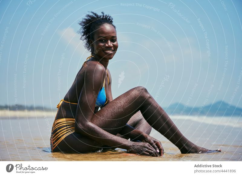 Sinnliches schwarzes Modell im Badeanzug ruht am Meeresufer Badebekleidung Körper sinnlich heiter feminin Schönheit Blauer Himmel Frau Afro-Look wolkig Inhalt