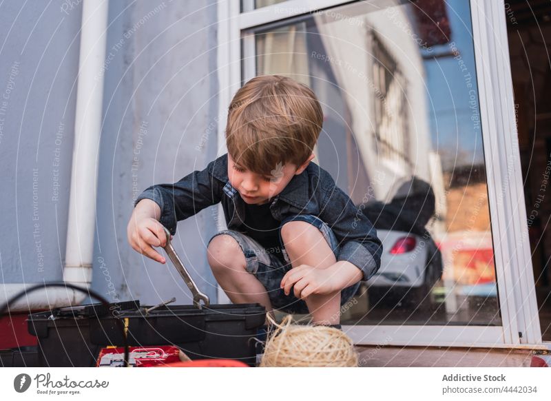 Junge nimmt bei Tageslicht einen Schraubenschlüssel aus der Schachtel herausnehmen neugierig Kindheit Werkzeug freie Zeit Instrument Garn Reflexion & Spiegelung