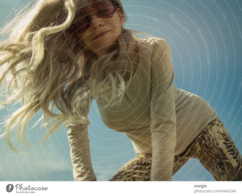 Eine blonde Frau mit Sonnenbrille schaut in die Kamera im Freien Sommer Weiblichkeit attraktiv langes Haar portraite herabschauen Dynamisch schlanke Frau