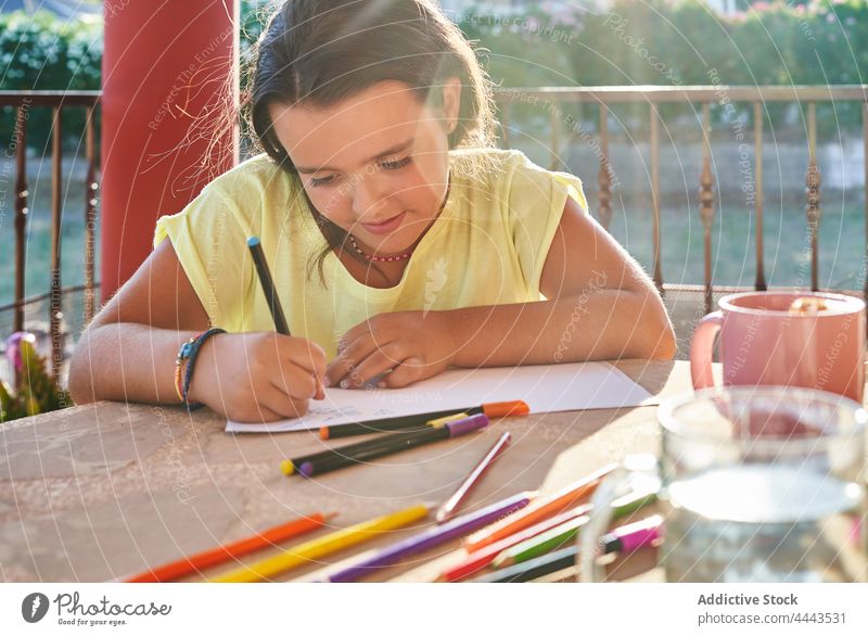 Konzentriertes Mädchen zeichnet auf Papier auf der Terrasse im Sonnenlicht zeichnen Tisch Kind kreativ positiv Hobby Konzentration Farbe lässig Kindheit heiter