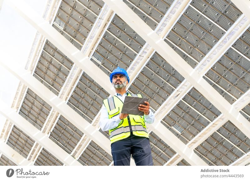 Ethnischer Bauunternehmer mit Tafel in der Nähe eines Solarkraftwerks Mann Tablette Arbeit solar professionell benutzend Apparatur Gerät Kraft Station Ökologie
