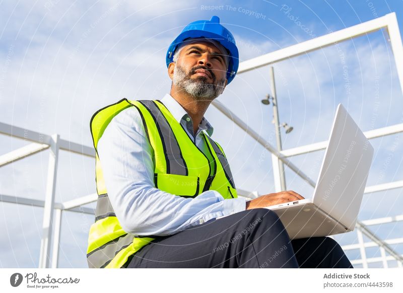 Inspektor arbeitet an einem Laptop unter einem modernen Solarkraftwerk Arbeit Internet Uniform Mann benutzend Apparatur Gerät Netbook Ingenieur Schutzhelm Weste