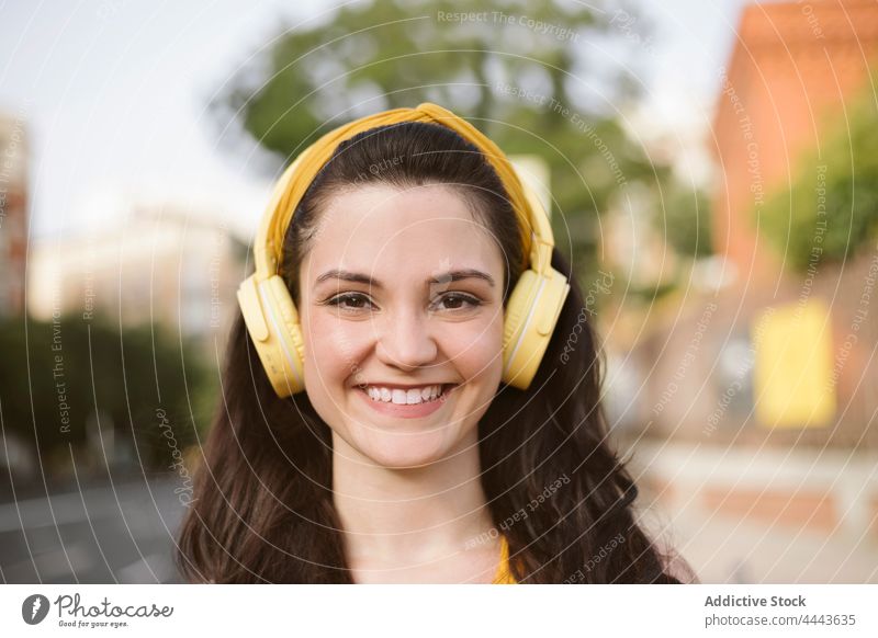 Fröhliche Frau mit Kopfhörern beim Gehen auf der Straße Musik zuhören Drahtlos positiv Hobby genießen sorgenfrei Gesang Apparatur Freude Audio tausendjährig