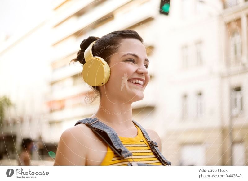 Fröhliche Frau mit Kopfhörern beim Gehen auf der Straße Musik zuhören Drahtlos positiv Hobby genießen sorgenfrei Gesang Apparatur Freude Audio tausendjährig