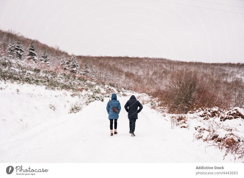 Freunde in Oberbekleidung, die tagsüber auf einem verschneiten Weg gegen einen verschneiten Hügel laufen Reisender Schnee Natur Winter Spaziergang Wald kalt