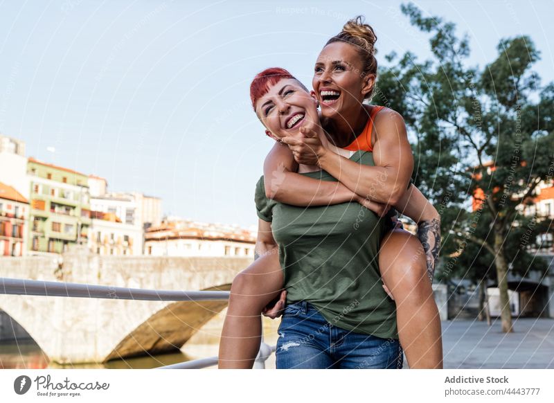 Glückliche Frau, die ihre homosexuelle Freundin huckepack auf einem Damm trägt Huckepack Spaß haben Lachen Partnerschaft sorgenfrei cool gleichgeschlechtlich
