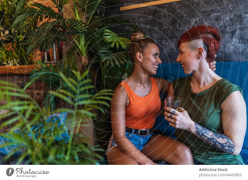 Lächelndes homosexuelles Paar mit Getränk umarmt auf Sofa zu Hause Freundin Umarmen Partnerschaft Liebe heiter gleichgeschlechtlich trinken reden Liege