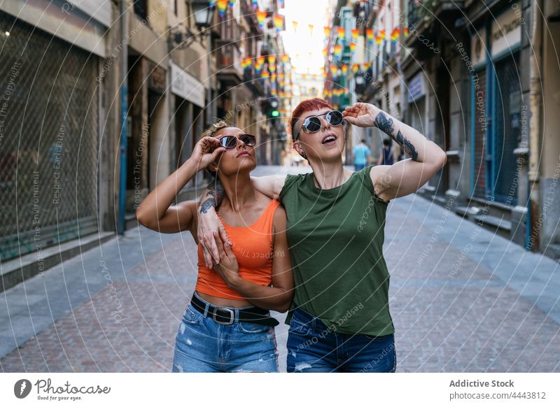 Lesbische Freundinnen mit modernen Sonnenbrillen umarmen sich auf dem städtischen Bürgersteig Umarmen lesbisch Tattoo Mode cool trendy überrascht Stadt Frauen