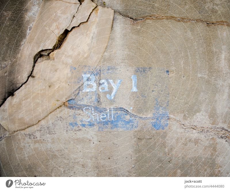 Bay 1 Shell Bezeichnung auf rissiger Mauer historisch alt Beschriftung Englisch Schriftzeichen Schablonenschrift Detailaufnahme Wort verwittert brüchig