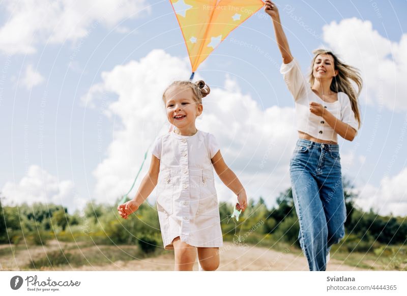 Ein lachendes kleines Mädchen und ihre Mutter laufen die Straße entlang zum Feld und lassen einen Drachen steigen. Mutter und Tochter haben Spaß zusammen Milan